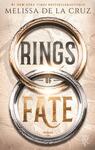 Das Buchcover zeigt zwei überlappende, kunstvoll gravierte Ringe – ein warmes Bronze/Gold oben, ein silbrig gravierter unten –, im Zentrum die Titelworte RINGS (oben in hohen, grauen Blockbuchstaben) und FATE (unten in großen, goldenen, strukturierten Kapitalen) getrennt durch ein kleines „of“. Im Hintergrund beige, kartografische Linien und eine mystische, epische Stimmung. Oben der Autorenname Melissa de la Cruz.