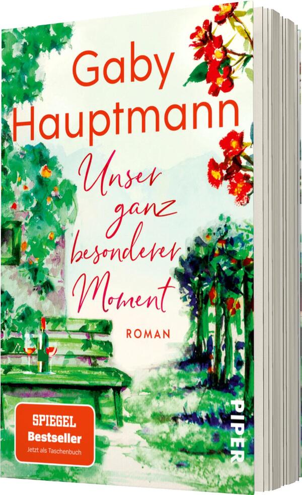 Das Buchcover zeigt eine idyllische Gartenszene mit bunten Blumen in Rottönen und grünem Laub. In der oberen Hälfte prominent platziert, steht der Name der Autorin „Gaby Hauptmann“ in einer lebhaften Schriftart. Darunter befindet sich der Titel „Unser ganz besonderer Moment“ in geschwungener, roter Schrift. Am unteren Rand ist das Wort „Roman“ in einer schlichten Schriftgröße zu sehen. Die Farbtöne vermitteln eine harmonische und einladende Atmosphäre.