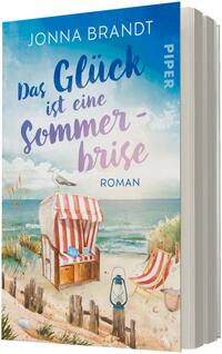 Das Buchcover zeigt eine idyllische Strandlandschaft mit hellem Sand, Dünen mit Gras, Meer und blauem Himmel. Im Vordergrund ein rot-weiß gestreifter Strandkorb, ein rot-weiß gestreifter Liegestuhl, Laterne und eine Möwe auf der Korblehne. Der Titel „Das Glück ist eine Sommerbrise“ steht groß in blauer bis lavendelfarbener, kalligrafischer Schrift; oben der Autorname „Jonna Brandt“, unten kleingedruckt „Roman“.