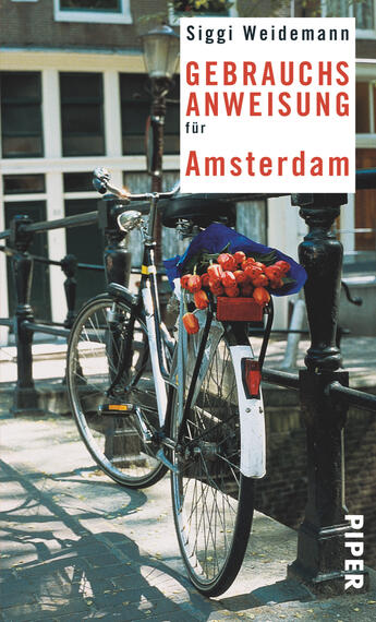 Das Buchcover zeigt ein Fahrrad, das an einem Kanal in Amsterdam abgestellt ist. Im Fahrradkorb befinden sich frische Blumen. Der Hintergrund ist hell gehalten, mit traditionellen, hellen Gebäuden in sanften Tönen. Der Titel „GEBRAUCHSANWEISUNG für Amsterdam“ steht in kräftigem Rot und klarer, serifenloser Schrift. Der Autor „Siggi Weidemann“ ist in einer schlichten Schriftart oben platziert. Die Gesamtatmosphäre vermittelt einen entspannten, einladenden Eindruck der Stadt.