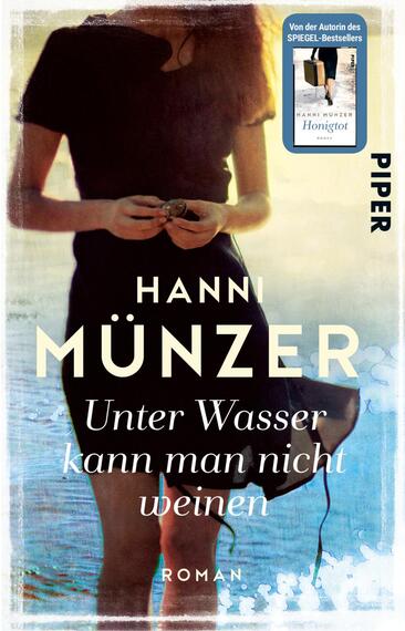 Das Buchcover zeigt eine Frau in einem langen schwarzen Kleid, die am Ufer eines Gewässers steht und eine Muschel in den Händen hält. Der Hintergrund ist in sanften Blau- und Hellgrautönen gehalten, was eine ruhige und melancholische Atmosphäre erzeugt. Der Titel „Unter Wasser kann man nicht weinen“ ist in eleganter, weißer Schrift platziert, während der Name der Autorin „Hanni Münzer“ in großem, auffälligem, schwarzem Font darüber steht. Das Verlagslogo „PIPER“ ist in der rechten oberen Ecke abgebildet.