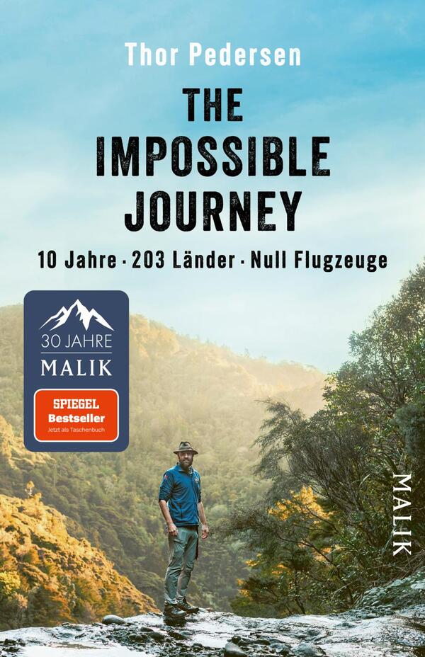 Das Buchcover zeigt eine Berglandschaft mit üppigem, grünem Bewuchs im Hintergrund. Im Vordergrund steht ein Mann in einem blauen Hemd und einer grauen Hose, der nachdenklich in die Ferne blickt. Der Titel „THE IMPOSSIBLE JOURNEY“ erscheint in großen, schwarzen Buchstaben, während die Untertitel „10 Jahre · 203 Länder · Null Flugzeuge“ in kleinerer Schrift darunter platziert sind. Der Name des Autors, Thor Pedersen, ist ebenfalls prominent oben auf dem Cover zu sehen. Die Gesamtatmosphäre vermittelt Abenteuerlust und Entdeckergeist.