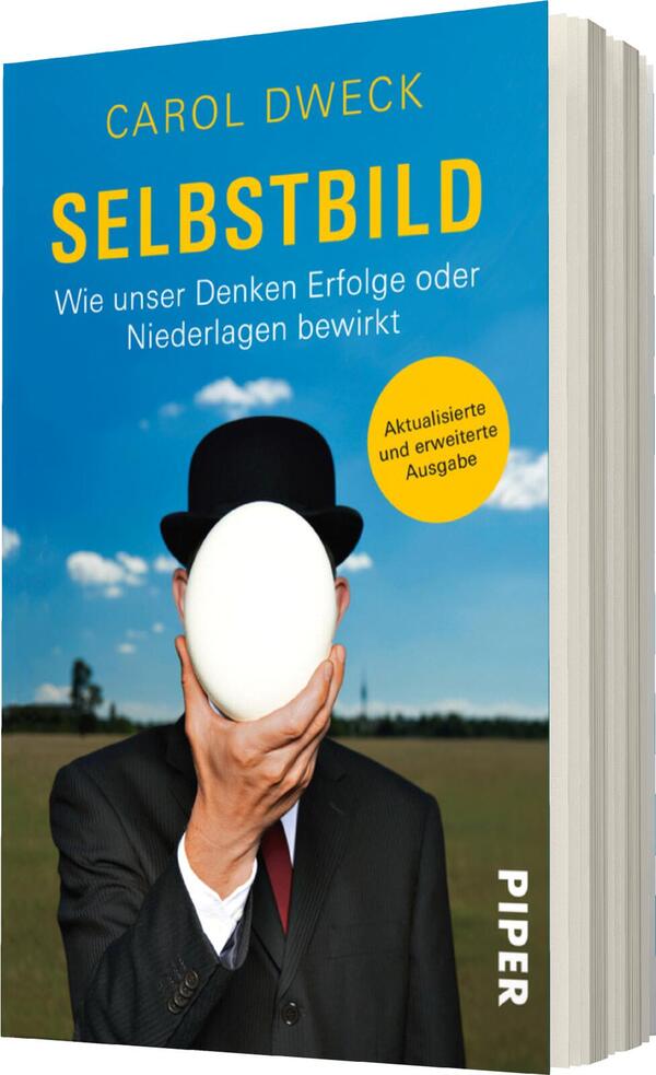 Das Buchcover zeigt einen Mann im Anzug mit einem Zylinder, der ein großes, weißes Ei in den Händen hält. Der Hintergrund ist eine weite, grüne Landschaft unter einem klaren Himmel. Der Titel „SELBSTBILD“ steht in großen, gelben Buchstaben oben auf dem Cover. Darunter befindet sich der Untertitel „Wie unser Denken Erfolge oder Niederlagen bewirkt“ in grauer Schrift. Ein Rundsymbol in Orange mit der Aufschrift „Aktualisierte und erweiterte Ausgabe“ ist ebenfalls abgebildet.