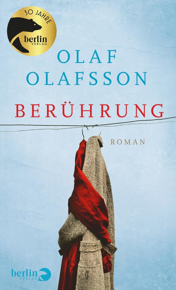 Das Buchcover zeigt einen hellblauen Hintergrund, auf dem zwei Kleidungsstücke an einem Draht hängen: ein grauer Mantel und ein rotes Tuch. Der Titel „Berührung“ steht in großen, rot- und blau gefärbten Buchstaben, während der Autor „Olaf Olafsson“ in blauen, etwas kleineren Buchstaben über dem Titel platziert ist. Am oberen Rand des Covers befindet sich ein goldenes Emblem mit dem Schriftzug „30 Jahre“, das den Verlag würdigt. Insgesamt vermittelt das Cover eine ruhige, nachdenkliche Atmosphäre.