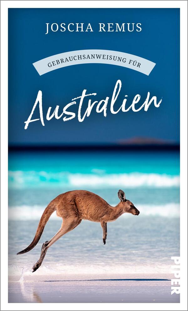 Das Buchcover zeigt einen Känguru, das über einen hellen Sandstrand springt, im Hintergrund sind sanfte Wellen und ein klarer blauer Himmel zu sehen. Der Titel „Australien“ hebt sich in einer verspielten, weißen Schrift ab, während der Untertitel „Gebrauchsanweisung für“ in einer geschwungenen grauen Schrift darüber angeordnet ist. Oben steht der Autorennamen „JOSCHA REMUS“ in klarer, blauer Schrift. Die Farbgestaltung vermittelt eine fröhliche, einladende Atmosphäre.