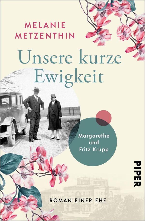 Das Buchcover zeigt einen sanften hellen Hintergrund, auf dem sich verspielte Blumen in Rosa und Türkis entfalten. Im oberen Bereich steht der Titel „Unsere kurze Ewigkeit“ in einer eleganten, hellblauen Schrift von Melanie Metzenthins. Darunter wird „Margarethe und Fritz Krupp“ in einem runden, grünen Element platziert. Ein historisches Foto von zwei Personen, gekleidet in altertümliche Kleidung, sowie ein Auto fügen dem Design nostalgische Elemente hinzu. Unten rechts ist das Verlagslogo „PIPER“.