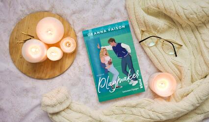 "Playmaker" liegt auf einer Decke. Daneben brennen Kerzen. Rechts liegen eine Strickdecke und eine Brille.