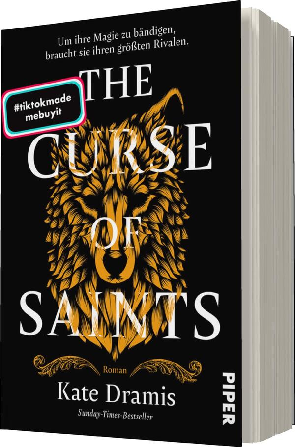 Das Buchcover zeigt einen schwarzen Hintergrund, auf dem ein majestätischer, golden gefärbter Wolfskopf in der Mitte abgebildet ist. Darüber prangt in großen, weißen Buchstaben der Titel „THE CURSE OF SAINTS“. Darunter steht in kleinerer Schrift „Roman“ und der Name der Autorin, Kate Dramis, gefolgt von der Angabe „Sunday-Times-Bestseller“. Ein bunter Sticker mit der Aufschrift „#tiktokmade“ ist in der oberen linken Ecke platziert. Die Gestaltung vermittelt eine mystische und kraftvolle Atmosphäre.