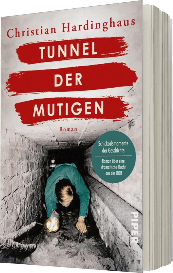 Das Buchcover zeigt eine düstere Tunnel-Szene, in der ein behelmter Mensch mit einer Lampe auf dem Boden hockt. Der Titel „TUNNEL DER MUTIGEN“ erscheint prominent in roten, dynamischen Buchstaben auf weißem Hintergrund. Der Schriftzug „Roman“ befindet sich in kleinerer Schrift unter dem Titel. Am unteren Rand des Covers steht in einer grünen Sprechblase der Zusatz „Schicksalsmomente der Geschichte“ sowie „Roman über eine dramatische Flucht aus der DDR“.