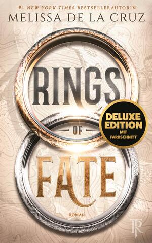 Das Buchcover zeigt den Titel in zwei ineinander gesetzten, ornamental verzierten Ringen – ein oberer goldener Ring mit dem Wort RINGS in kräftiger Großschrift und ein unterer silberner Ring mit dem Wort FATE in goldener Serifenschrift. Hintergrund hellbeige mit feinem Karten- und Ornamentmuster, oben Autorinname Melissa de la Cruz. Atmosphäre geheimnisvoll, antik, episch. Runder schwarzgoldener Button mit dem Text „DELUXE EDITION MIT FARBESCHNITT“.