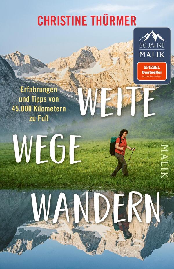 Das Buchcover zeigt eine Wanderin in einer malerischen Berglandschaft. Sie trägt einen Rucksack und hält einen Wanderstock, während sie auf eine grüne Wiese mit Bergen im Hintergrund blickt. Der obere Teil ist in sanften Blau- und Grautönen gehalten, die die hohen Berge darstellen. Der Titel „WEITE WEGE WANDERN“ ist in großen, weißen Buchstaben platziert, die auffällig auf dem Cover stehen. Der Untertitel „Erfahrungen und Tipps von 45.000 Kilometern zu Fuß“ ist in kleinerer Schrift darunter zu lesen. Oben links prangt ein rotes Feld mit der Aufschrift „SPIEGEL Bestseller“.