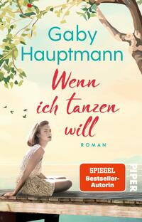 Das Buchcover zeigt eine junge Frau in hellgemustertem Kleid, die auf einem Holzsteg am Wasser sitzt, links oben ein blätterreicher Baum, einige kleine Vögel am Himmel; die Szene strahlt eine ruhige, sommerliche Stimmung aus. Auf pastellfarbenem Hintergrund steht oben in türkis die Autorin „Gaby Hauptmann“, mittig der Titel in roten, handschriftlichen Lettern „Wenn ich tanzen will“, unten klein „ROMAN“ in türkis. Oranger Button mit dem Text „SPIEGEL Bestseller-Autorin“.
