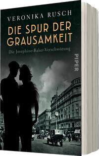 Das Buchcover zeigt eine düstere, stilisierte Stadtansicht im Hintergrund mit historischer Architektur und in blassen Grautönen gehalten. Im Vordergrund stehen zwei silhouettenhafte Figuren, die in die gleiche Richtung blicken. Der Titel „DIE SPUR DER Grausamkeit“ erscheint in großen, goldenen Buchstaben, während der Untertitel „Die Josephine-Baker-Verschwörung“ in einer kleineren Schrift darunter steht. Der Autor „VERONIKA RUSCH“ ist oben auf dem Cover platziert. Die Gesamtkomposition vermittelt eine geheimnisvolle und spannende Atmosphäre.