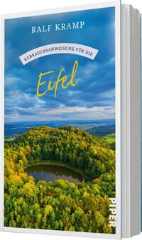 Das Buchcover zeigt eine malerische Landschaft der Eifel mit sanften Hügeln und bewaldeten Flächen, die in verschiedenen Grüntönen leuchten. In der Mitte des Covers ist ein kleiner, ruhiger See zu sehen, umgeben von einer dichten Baumgruppe. Der Himmel ist teilweise bewölkt und strahlt in sanften Blautönen. Oben befindet sich der Titel „Gebrauchsanweisung für die Eifel“ in einer eleganten, geschwungenen Schriftart, gefolgt vom Autorennamen „Ralf Kramp“ in einer klaren, serifenlosen Schrift.