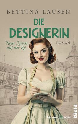 Das Buchcover zeigt eine junge Frau mit lockigem, rotem Haar in einem eleganten, pastellgrünen Kleid. Sie hält einen Notizblock in der Hand und lächelt, während sie in die Kamera blickt. Im Hintergrund ist eine historische Gebäudestruktur zu sehen. Der Titel „DIE DESIGNERIN“ ist in großen, matten grünen Buchstaben geschrieben, darunter steht „Neue Zeiten auf der Kö“ in kleinerer, grauer Schrift. Die Atmosphäre vermittelt ein Gefühl von Nostalgie und Kreativität.