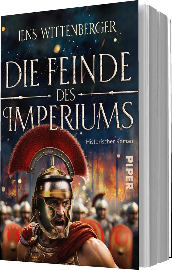 Das Buchcover zeigt einen kriegerischen römischen Soldaten mit einer markanten roten Helmzier. Der Hintergrund ist in dunklen Farben gehalten und zeigt schemenhafte Figuren von weiteren Soldaten, die eine dramatische Atmosphäre erzeugen. Der Titel „Die Feinde des Imperiums“ ist in großen, goldenen Buchstaben prominent platziert, während der Untertitel „Historischer Roman“ in kleinerer, silberner Schrift darunter steht. Der Name des Autors, Jens Wittenberger, befindet sich oben auf dem Cover.