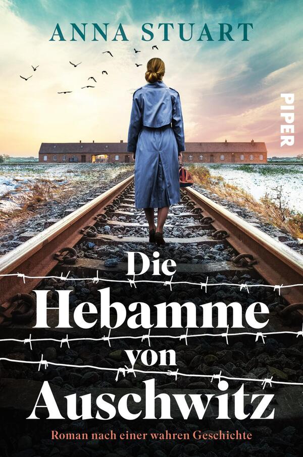 Das Buchcover zeigt eine Frau in einem blauen Mantel, die auf einem Bahngleis steht und zum Hintergrund blickt. Hinter ihr sind barrierefreie Zäune und verwitterte Gebäude zu erkennen, die eine bedrückende Atmosphäre erzeugen. Der Himmel ist von Wolken durchzogen und Vögel fliegen darüber. Der Titel „Die Hebamme von Auschwitz“ steht in großen, weißen Buchstaben, darunter der Zusatz „Roman nach einer wahren Geschichte“. Oben links ist der Name der Autorin „Anna Stuart“ in kleinerer Schrift zu sehen, das Verlagslogo ist rechts am Rand platziert.