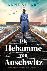 Das Buchcover zeigt eine Frau in einem blauen Mantel, die auf einem Bahngleis steht und zum Hintergrund blickt. Hinter ihr sind barrierefreie Zäune und verwitterte Gebäude zu erkennen, die eine bedrückende Atmosphäre erzeugen. Der Himmel ist von Wolken durchzogen und Vögel fliegen darüber. Der Titel „Die Hebamme von Auschwitz“ steht in großen, weißen Buchstaben, darunter der Zusatz „Roman nach einer wahren Geschichte“. Oben links ist der Name der Autorin „Anna Stuart“ in kleinerer Schrift zu sehen, das Verlagslogo ist rechts am Rand platziert.