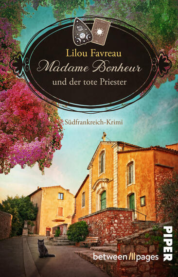 Das Buchcover zeigt ein ovales schwarzes Etikett mit goldener Zierlinie, darauf der Name Lilou Favreau und der Titel „Madame Bonheur und der tote Priester“ in goldener, elegante Schreibschrift; darunter klein die Angabe „Südfrankreich-Krimi“. Darüber zwei Tarotkarten und ein Amulett als Symbolik. Im Vordergrund ein sonniges, ockerfarbenes Dörfchen mit grünen Fensterläden, pink blühendem Baum, türkisblauem Himmel und einer schwarzen Katze auf dem Pflaster, ruhig und leicht mysteriös.