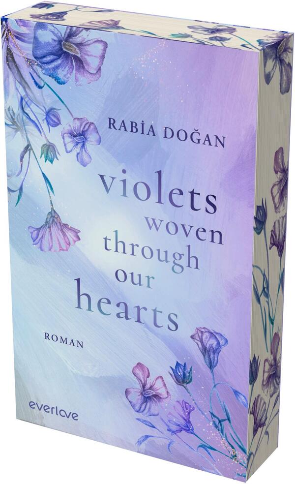 Das Buchcover zeigt einen pastelligen, violett-blauen Aquarellhintergrund mit handgezeichneten, zarten Veilchen und Blütenranken oben links und unten rechts. Mittig steht der Titel in serifenloser, eleganter Schrift: „violets woven through our hearts“, darüber der Autorname „Rabia Doǧan“ in Großbuchstaben, unten links das Genre „Roman“. Farben: Lavendel, Flieder und Hellblau; Atmosphäre: ruhig, poetisch und melancholisch.