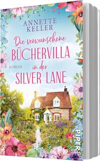 Das Buchcover zeigt eine malerische Buchvilla umgeben von üppig blühenden Gärten und einem strahlend blauen Himmel. Der Titel „Die verwunschenen Büchervilla in der Silver Lane“ ist in verspielter, pinker Schrift oben platziert, während der Zusatz „Roman“ in schlichter, goldener Schrift am unteren Rand steht. Sanfte Farben und eine einladende Atmosphäre schaffen ein Gefühl von Romantik und Entdeckung.