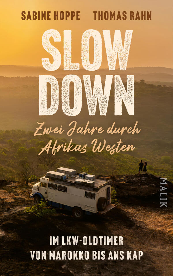 Das Buchcover zeigt eine Szene im goldenen Abendlicht: oben die Autorennamen Sabine Hoppe und Thomas Rahn in blockiger, braun‑goldener Versaltypografie. Zentral prangt der Titel SLOW DOWN in großen, rauen weißen Großbuchstaben, darunter die kursiv-handschriftliche Zeile „Zwei Jahre durch Afrikas Westen“. Im Vordergrund ein weißer LKW-Oldtimer auf einem Felsen, zwei winzige Silhouetten, weiter Blick über nebelige Hügel, ruhige, abenteuerliche Atmosphäre.