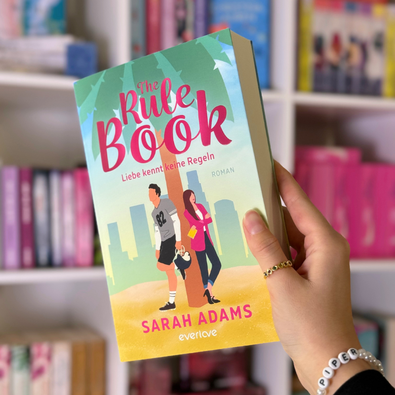 „The Rule Book“ von Sarah Adams wird vor einem Bücherregal gehalten