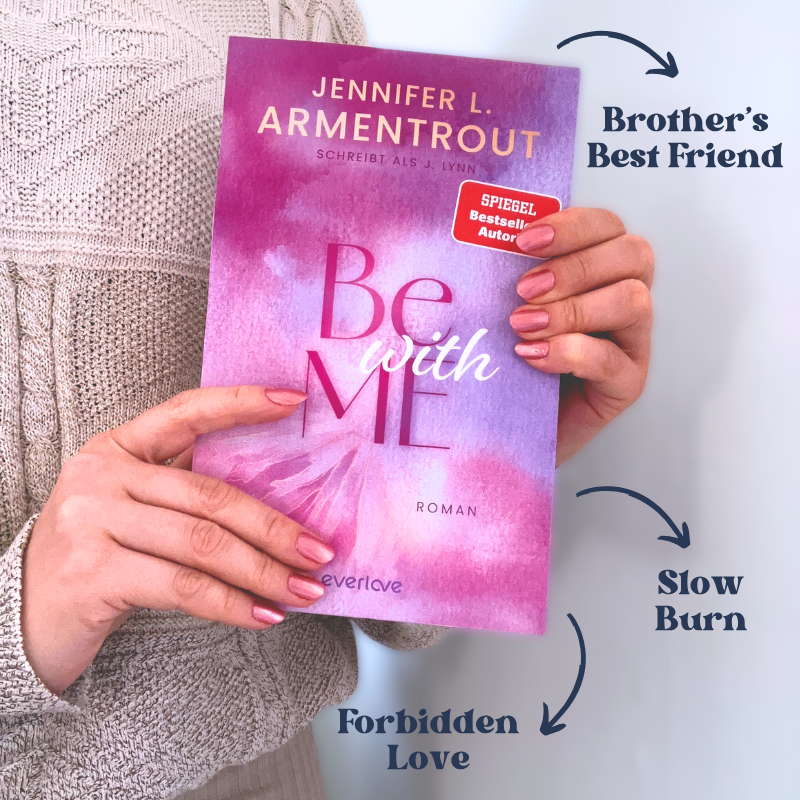 „Be with Me“ von Jennifer L. Armentrout wird vor einem beigen Strickpullover gehalten. Daneben stehen die Tropes „Forbidden Love“, „Slow Burn“ und „Brother's Best Friend“