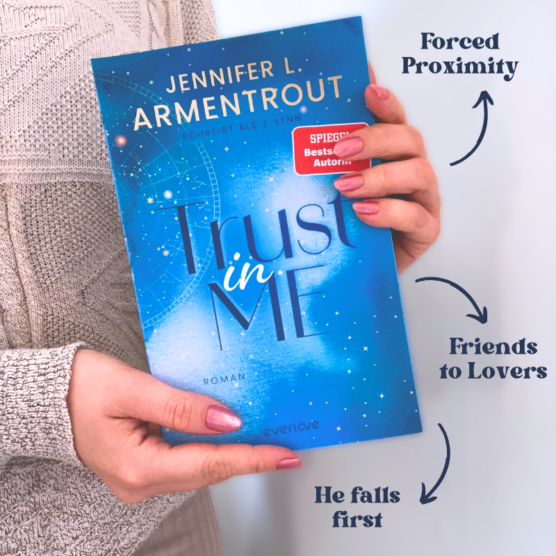 „Trust in Me“ von Jennifer L. Armentrout wird vor einem beigen Strickpullover gehalten. Die Tropes „Forced Proximity“, „Friends to Lovers“ und „He Falls First“ stehen daneben.