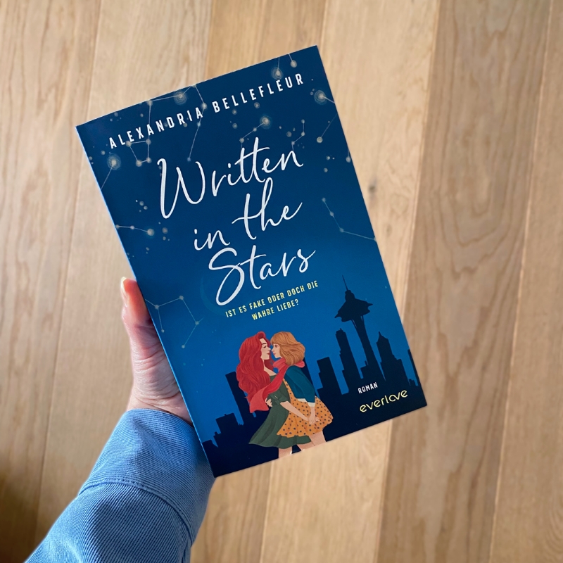 Eine Hand hält „Written in der Stars“ über einem Holzboden