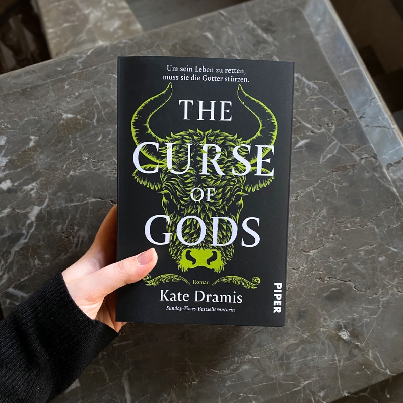 „The Curse of Gods“ wird vor einem dunklen Marmorstein gehalten