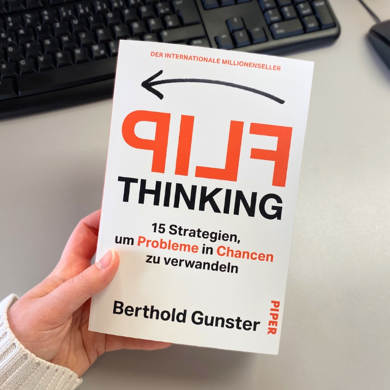 „Flip Thinking“ wird von einer Hand gehalten, im Hintergrund ist eine Tastatur zu sehen