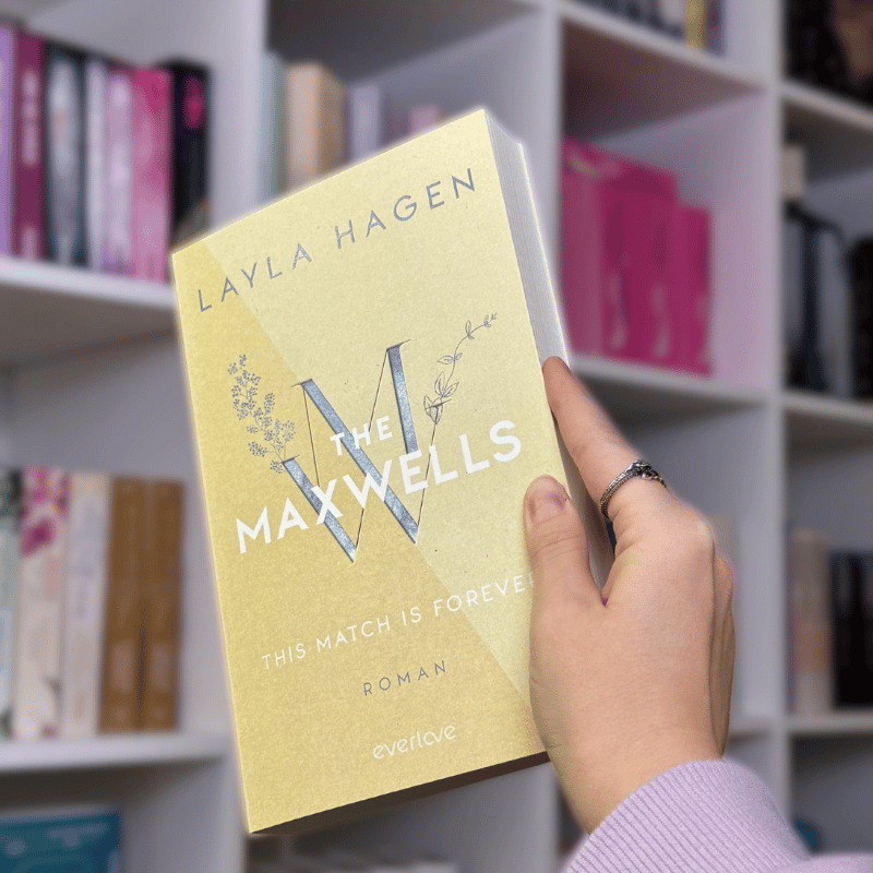 „The Maxwells – This Match Is Forever“ von Layla Hagen wird vor ein Bücherregal gehalten