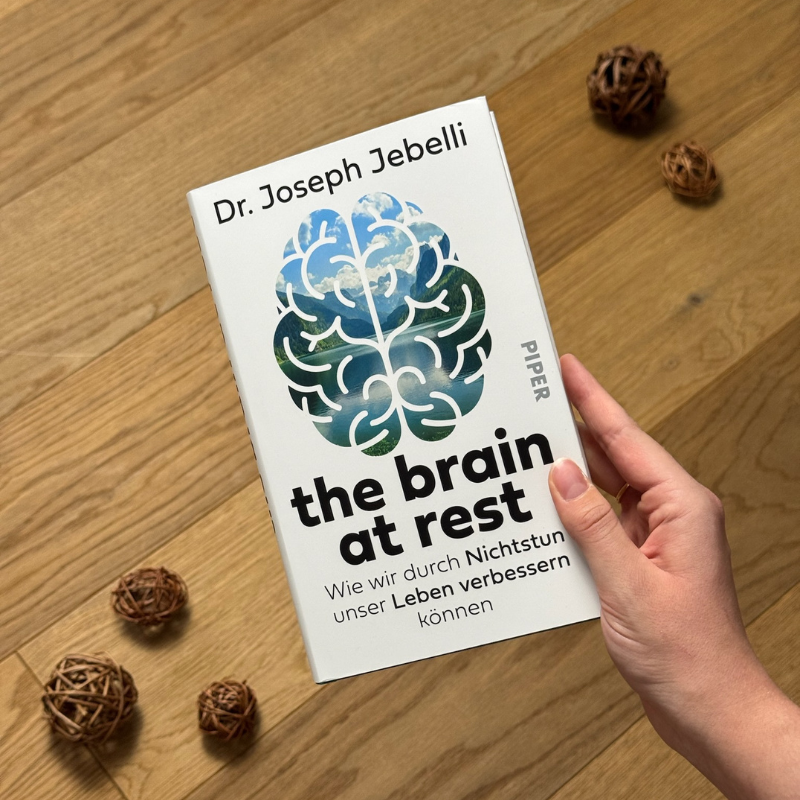 „The Brain at Rest“ von Dr. Joseph Jebelli in einer Hand über einem Holzboden gehalten.
