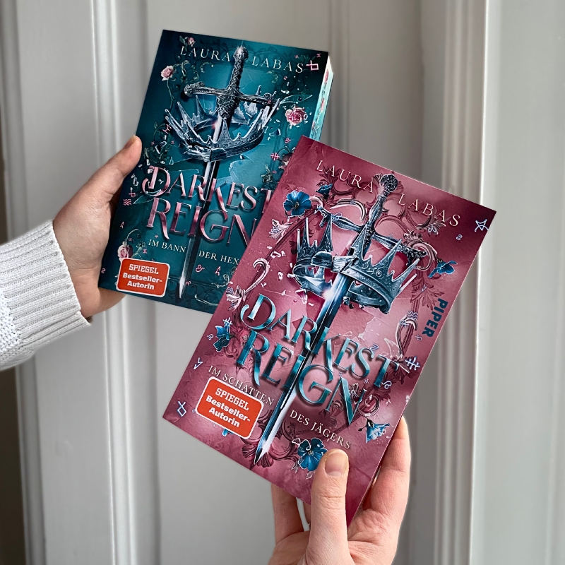 Band 1 und 2 der „Darkest Reign“-Dilogie werden vor vor weißem Hintergrund hochgehalten