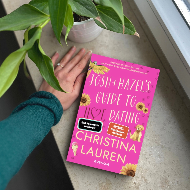"Josh and Hazel's Guide to not dating" liegt auf einer Fensterbank. Daneben stützt sich eine Hand ab und eine Zimmerpflanze steht daneben.