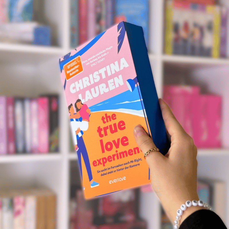 „The True Love Experiment“ von Christina Lauren wird vor einem Bücherregal gehalten