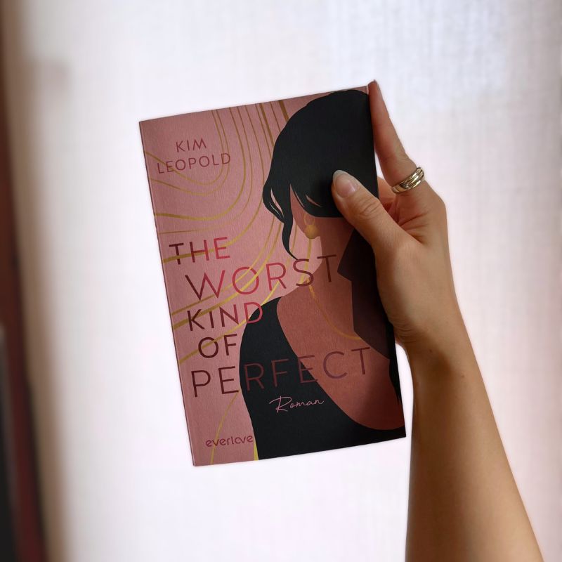 "The Worst Kind of Perfect" von Kim Leopold wird in einer Hand vor einer weißen Wand gehalten gehalten.