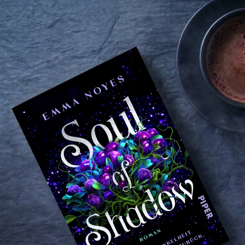 „Spul of Shadow" liegt auf einem dunkelgrauen Untergrund. Daneben steht eine Tasse mit Kaffee.