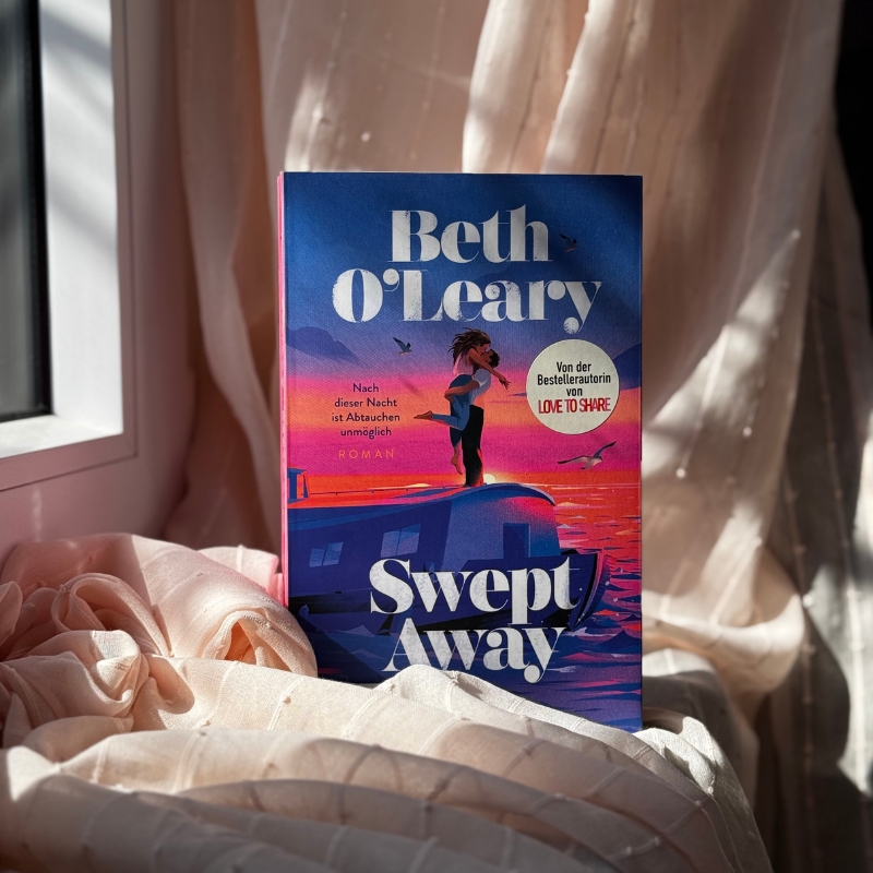 "Swept away" steht auf einer Fensterbank. Dahinter und darunter hängt bzw. liegt ein rosafarbener Vorhang. 
