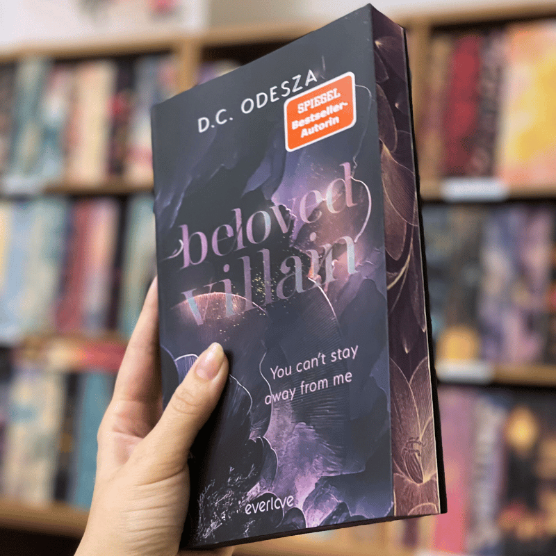 „Beloved Villain“ von D.C. Odesza wird vor einem Bücherregal gehalten