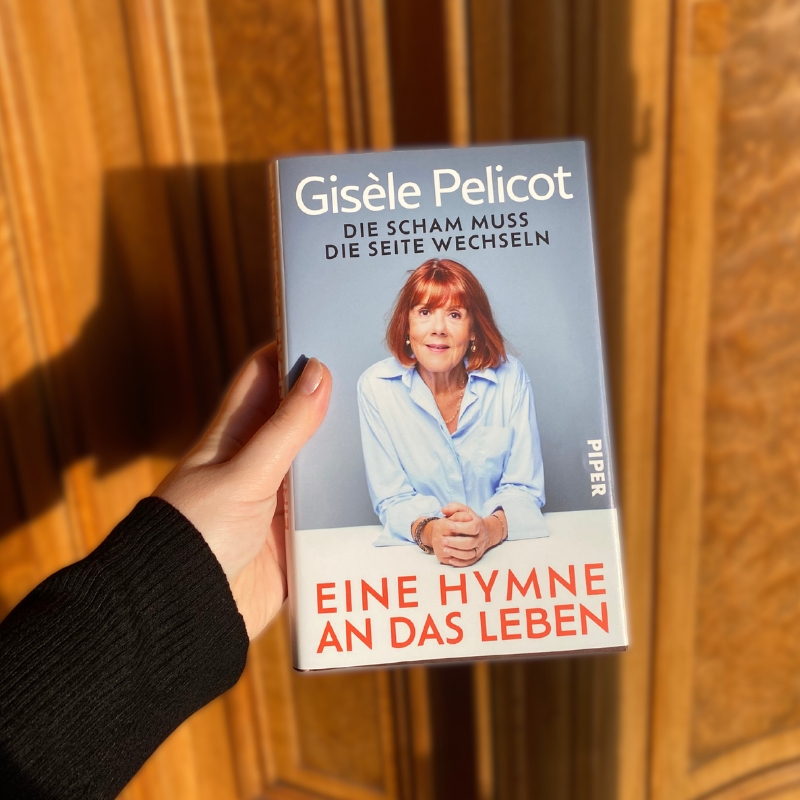 Eine Hand hält „Eine Hymne an das Leben“ vor einer Holztür