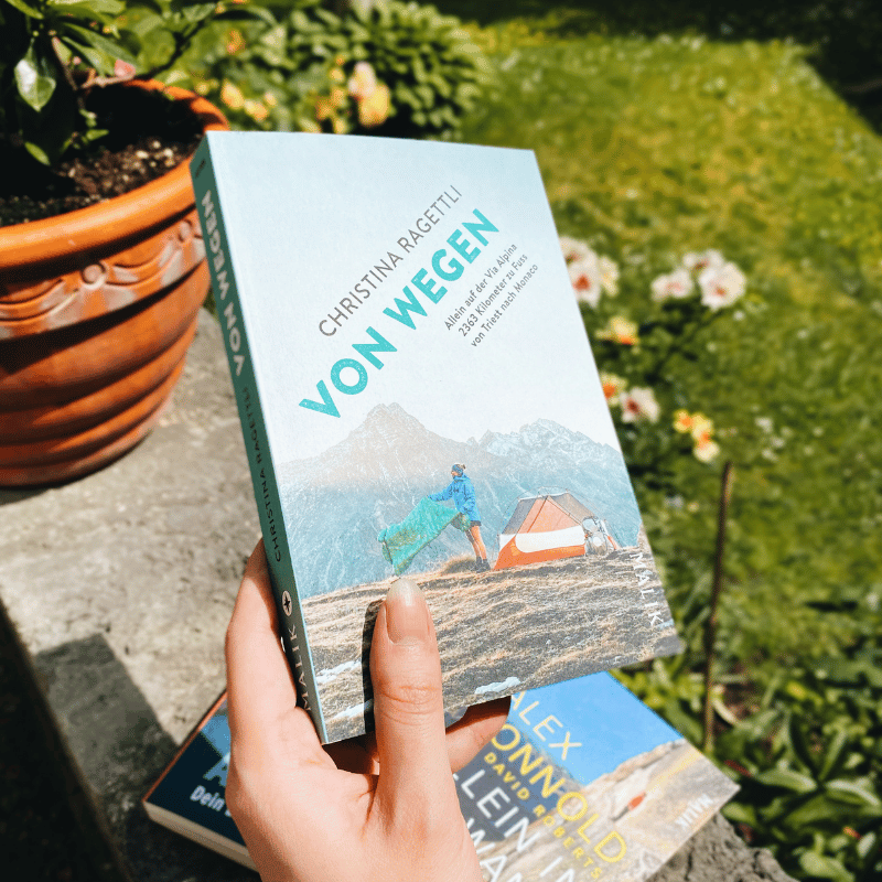 „Von Wegen“ von Christina Ragettli wir von einer Hand gehalten. Im Hintergrund ist ein Garten