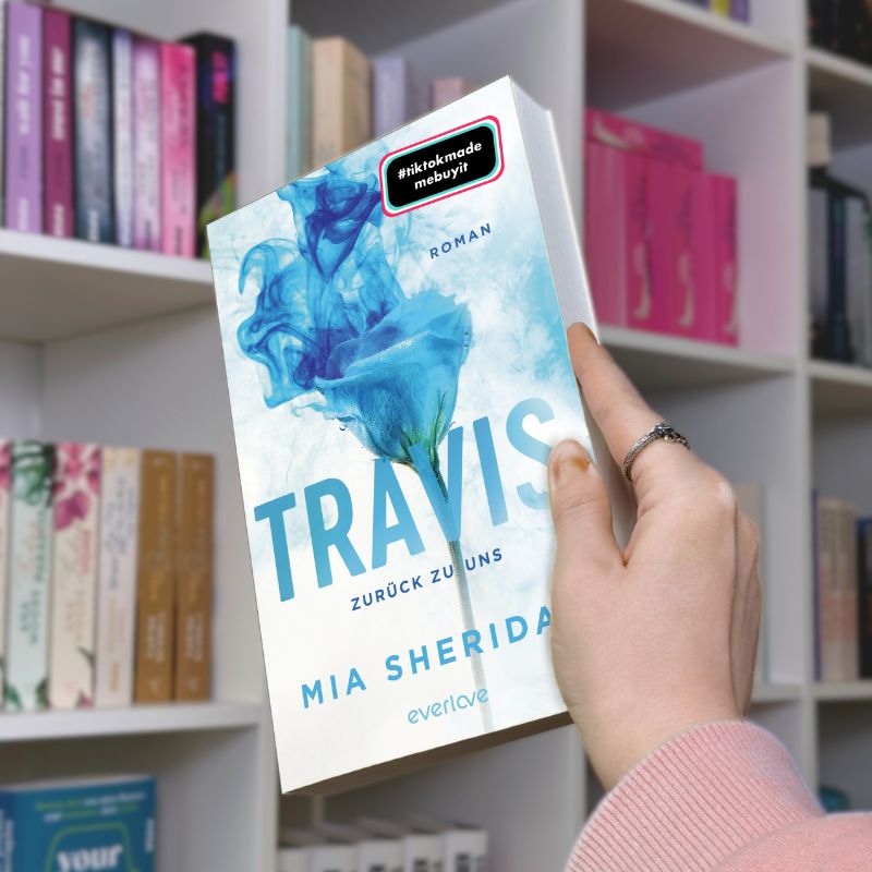 "Travis" von Mia Sheridan wird vor einem Bücherregal gehalten.