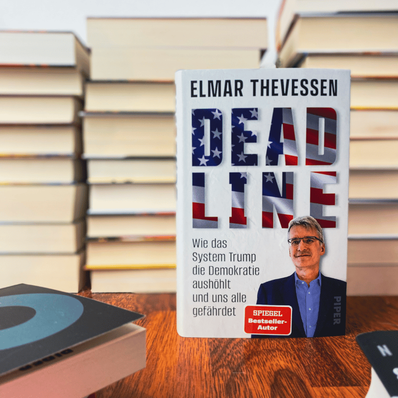 „Deadline – Wie das System Trump die Demokratie aushöhlt und uns alle gefährdet“ von Elmar Theveßen wird vor einem Bücherstapel präsentiert.