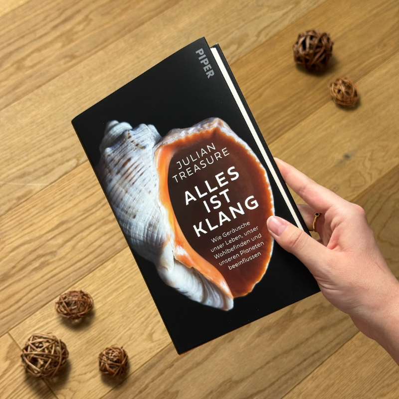 „Alles ist Klang“ von Julian Treasure in einer Hand über einem Holzboden gehalten.