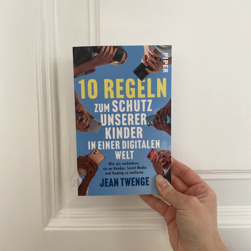 "10 Regeln zum Schutz unserer Kinder in einer digitalen Welt" wird von einer Hand vor eine weiße Wand gehalten