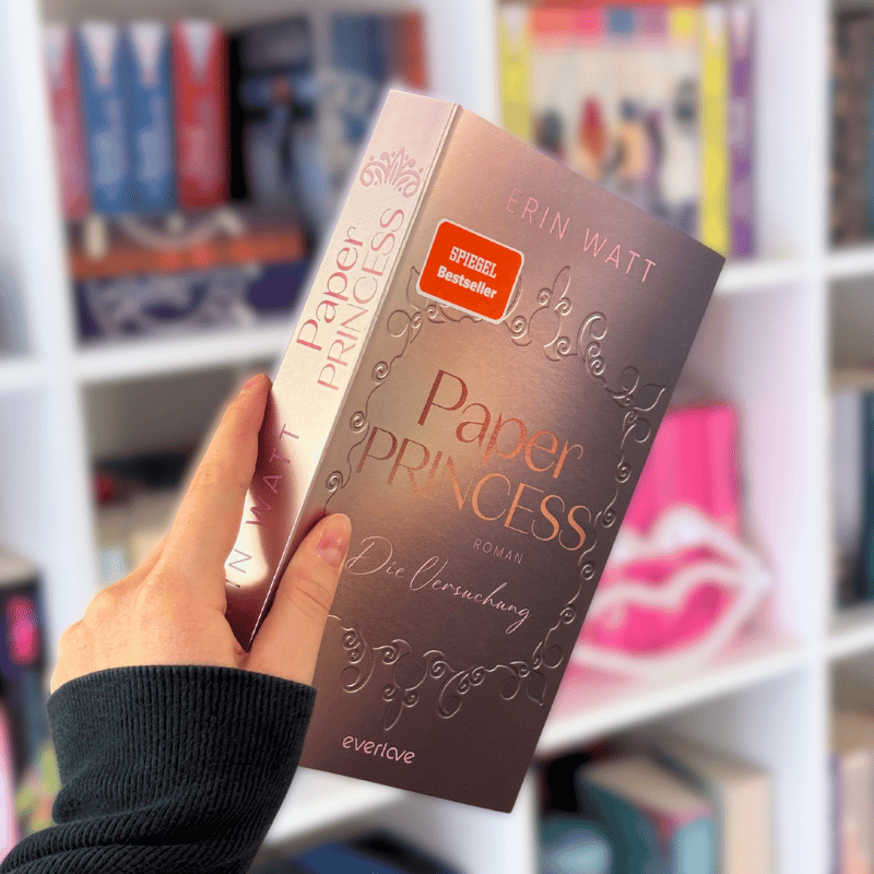 „Paper Princess“ von Erin Watt wird vor einem Bücherregal gehalten