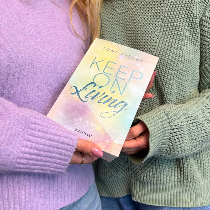 2 Personen halten „Keep on Living“ vor ihren farblich passenden Pullovern