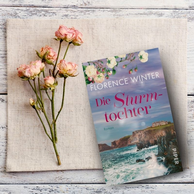 Florence Winter: Die Sturmtochter liegt auf einer beigen Tischdecke mit rosa Rosen